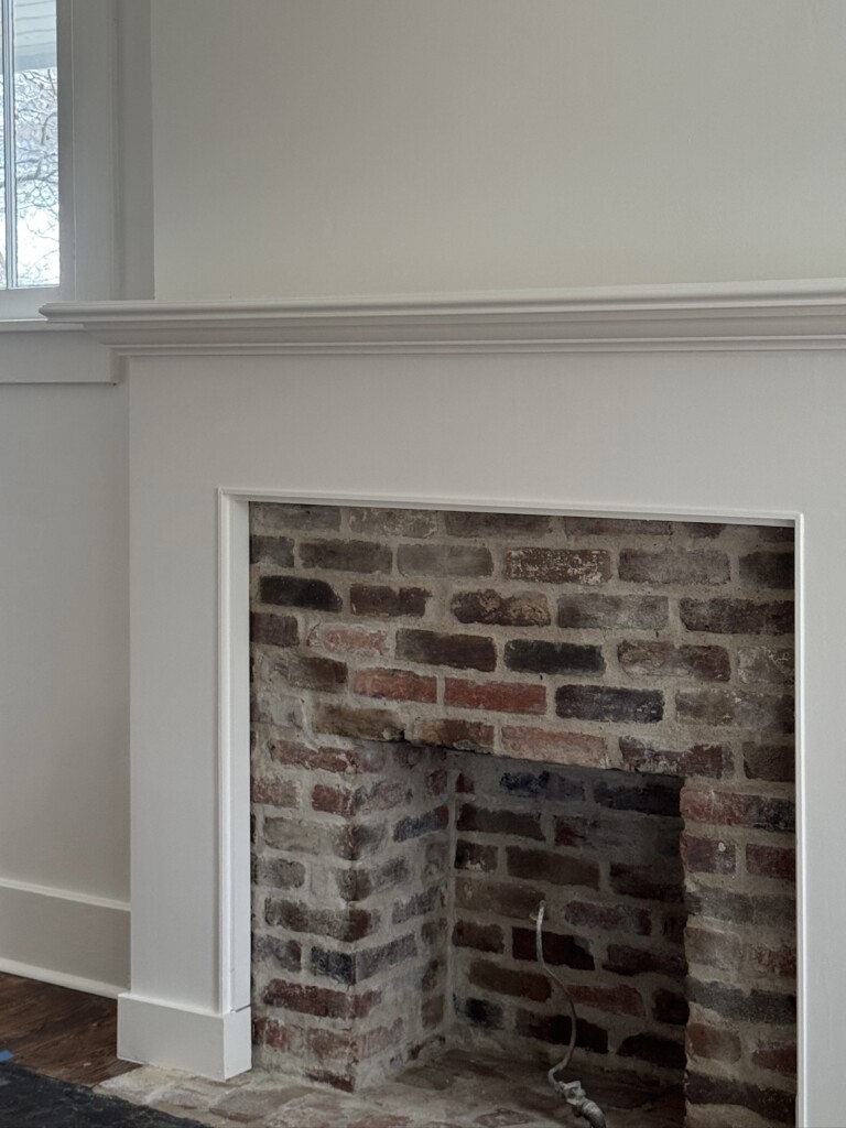 Brick fireplace renovation in progress with stripped wood mantel surround and exposed original brick firebox and hearth.