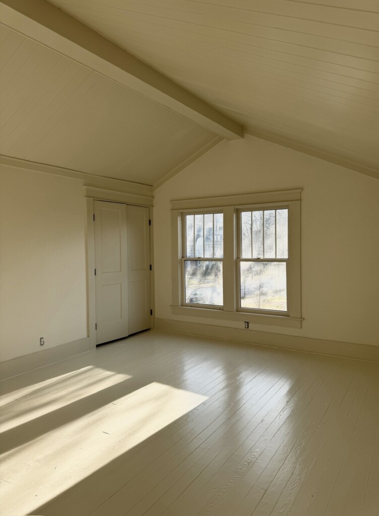 Bedroom with painted white wood floors, paneled walls, and a large window at the end