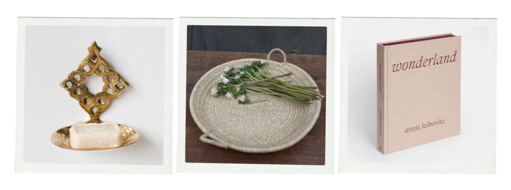 Three home accents featuring a brass soap dish with a decorative backplate, a woven tray holding fresh flowers, and a neutral-toned coffee table book titled “Wonderland” by Annie Leibovitz.
