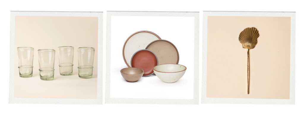 A set of everyday tabletop pieces including clear drinking glasses, neutral ceramic plates and bowls, and a brass spoon shaped like a shell.
