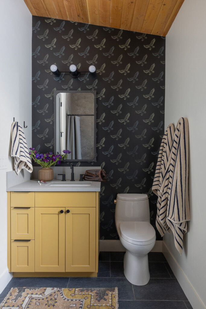 Small bathroom with yellow vanity, dark bird wallpaper, and striped towels for added pattern