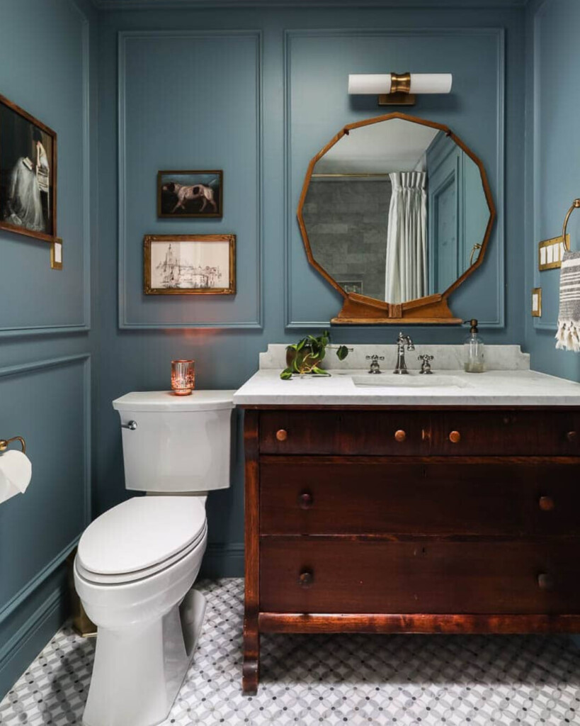 A bathroom with blue paneled walls, a warm wood vanity, brass fixtures, and a geometric tile floor, balancing classic materials with a bold color choice.