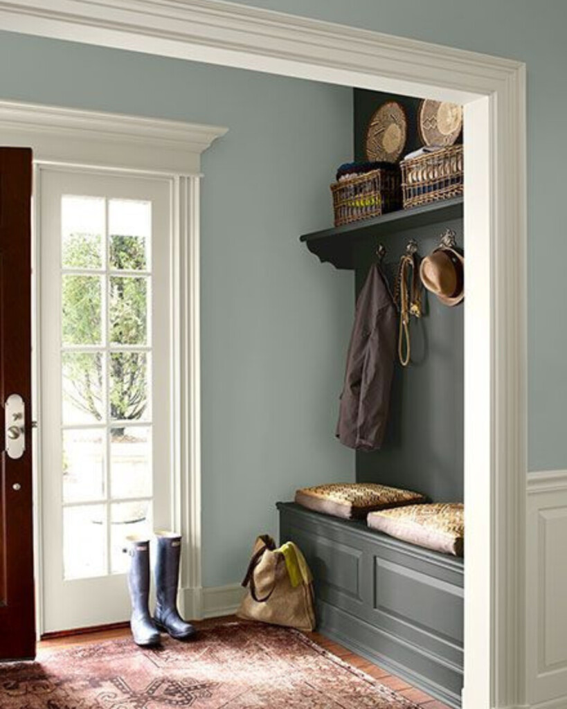A light, airy entryway with soft blue walls, a darker built-in bench, woven textures, and natural light creating contrast between tones.